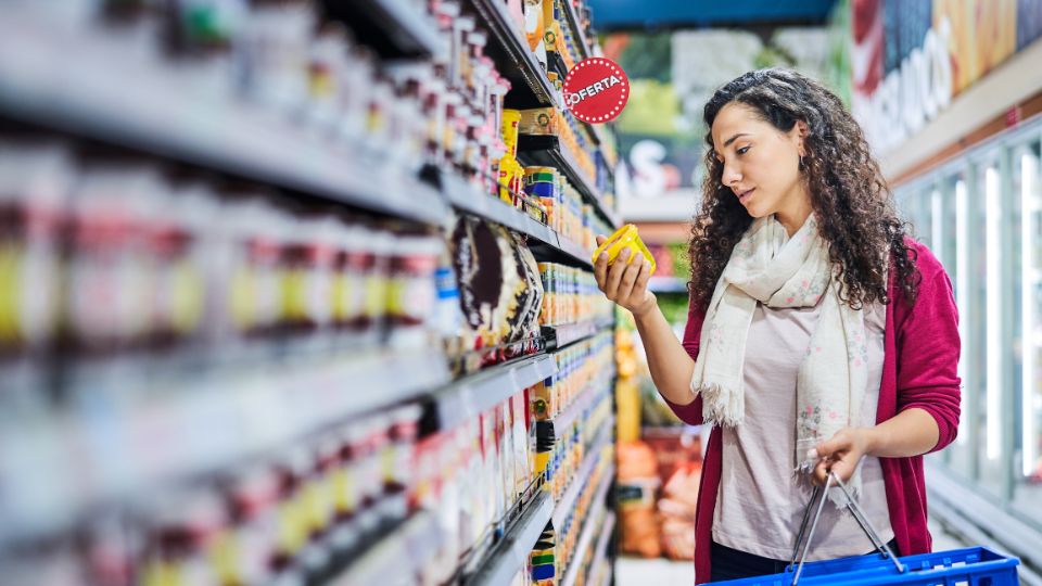 A photograph a woman in a food retail store. She is looking at a food product in a grocery store. 